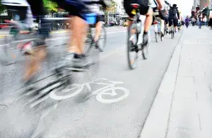 Auf diesem Bild sieht man einen Fahrradweg mit vielen Fahrradfahrern und Fahrradfahrerinnen. Das Bild ist verschwommen, weil die Fahrräder beim fahren Fotografiert wurden.