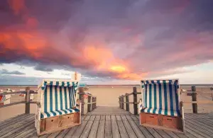 Das Foto zeigt zwei Strandkörbe. Im Hintergrund sieht man den Strand und einen Sonnenuntergang. 