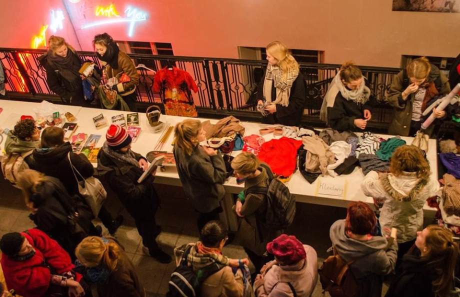 Jugendliche sind um einen langen Tisch versammelt, auf dem viele Kleidungsstücke ausgebreitet sind.