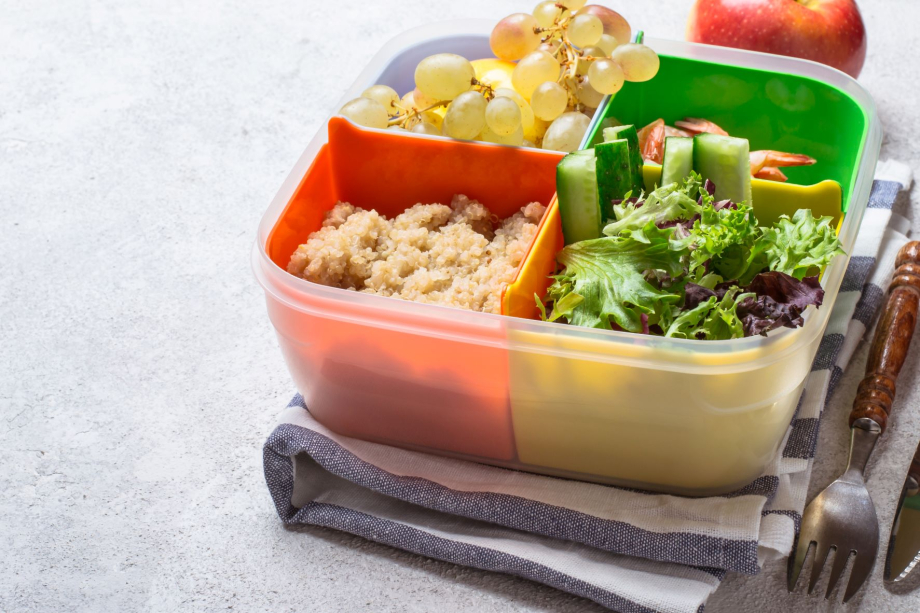 Das Bild zeigt eine gefüllte Essensbox mit Salat, Weintrauben und anderen Beilagen.