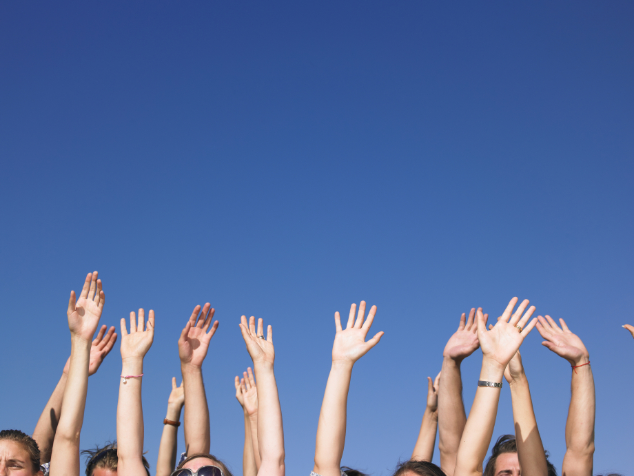 Das Foto zeigt gehobene Hände, die vor einem blauen Himmel winken. 