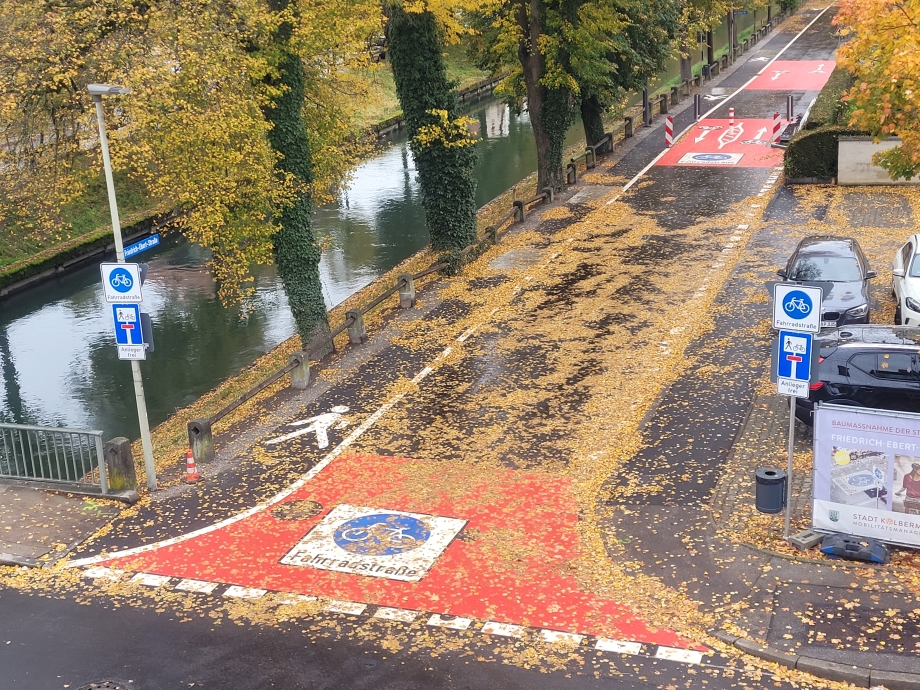 Luftbild der Einfahrt zur Fahrradstraße, am Rand ein Kanal und Herbstbäume, sowie Autos und Schilder