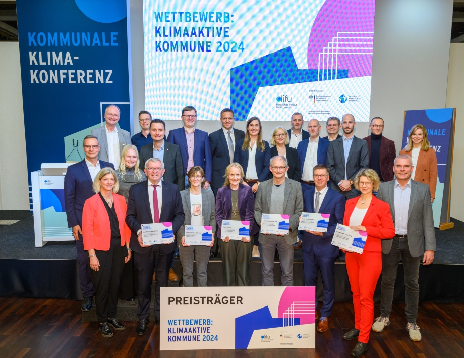 Die Teams der sechs ausgezeichneten Kommunen des Wettbewerbs „Klimaaktive Kommune 2024“ gemeinsam mit Gratulanten auf der Bühne der Kommunalen Klimakonferenz in Berlin