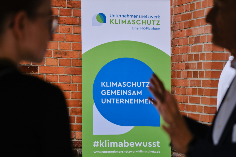 Ein Roll-Up-Banner des Unternehmensnetzwerks Klimaschutz steht vor einer Backsteinwand und trägt eine klimabewusste Aufschrift.