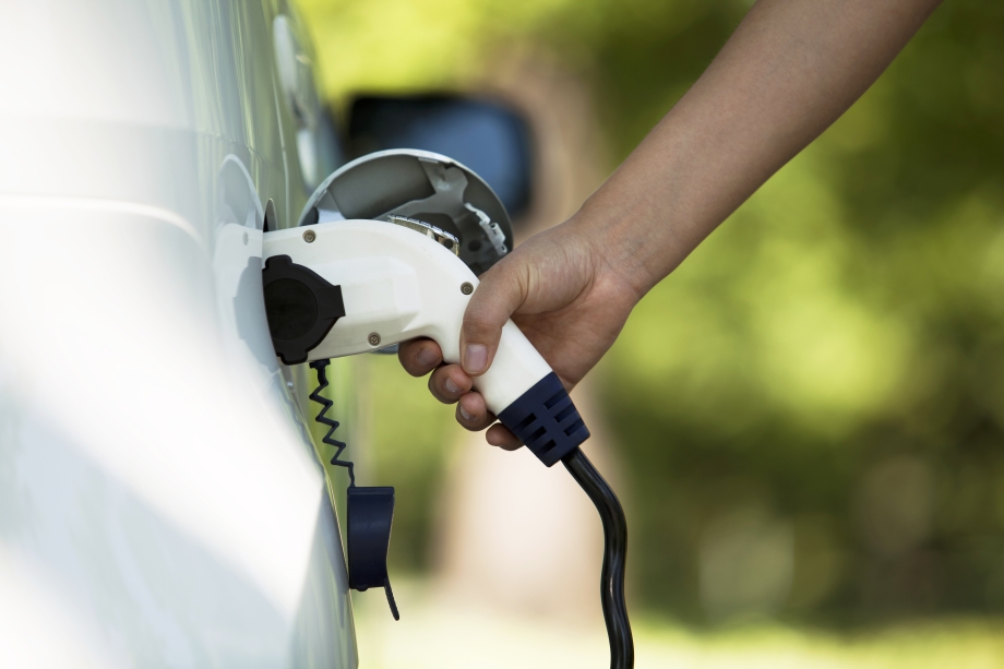 Nahaufnahme einer Hand, die ein Elektroauto an eine Ladestation anschließt.