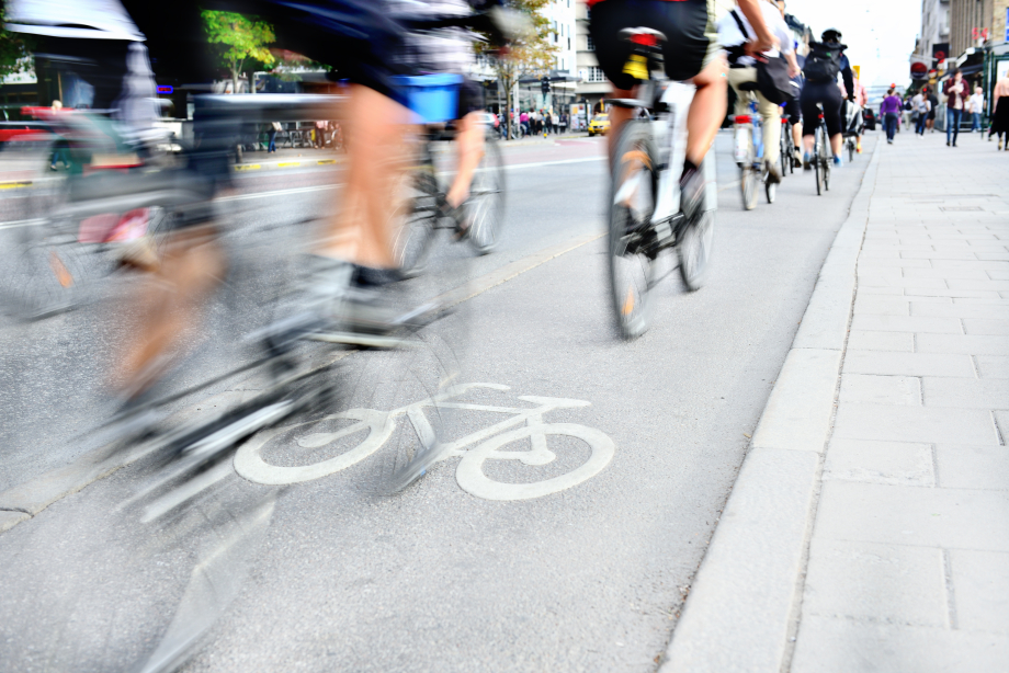 Auf diesem Bild sieht man einen Fahrradweg mit vielen Fahrradfahrern und Fahrradfahrerinnen. Das Bild ist verschwommen, weil die Fahrräder beim fahren Fotografiert wurden.