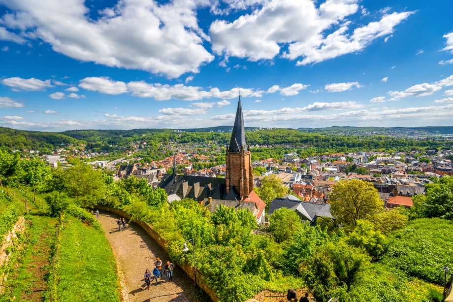 Kleine Stadt mit Kirchturm inmitten grüner Hügel unter blauem Himmel mit vereinzelten weißen Wolken