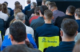 Menschen von hinten, sitzen dicht nebeneinander in einem Seminarraum. Eine Person in der Mitte trägt eine Weste mit der Aufschrift "Energie Scouts".