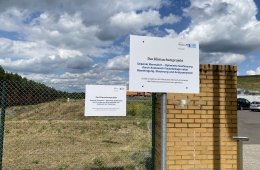 Schild am Zaun vor der Deponieanlage mit einer Beschreibung zum Projekt und den Logos der NKI und des BMWK