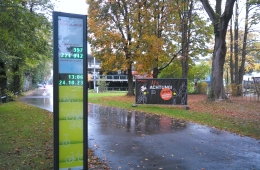 Eine Straße mit einer Säule, auf der die Anzahl der Fahrräder aufgeführt sind, im Hintergrund Herbstbäume und ein Gebäude