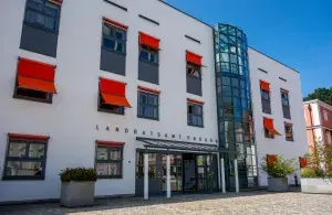 Außenansicht des Landratsamtes Passau, eines relativ modernen Verwaltungsgebäudes mit orangefarbenen Verschattungsvorrichtungen vor den Fenstern, vor blauem Himmel