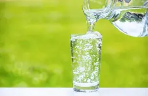 In ein Glas wird Wasser aus einem Krug eingegossen. Im Hintergrund ist eine Wiese zu sehen. 