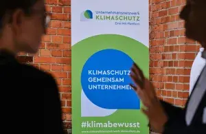 Ein Roll-Up-Banner des Unternehmensnetzwerks Klimaschutz steht vor einer Backsteinwand und trägt eine klimabewusste Aufschrift.