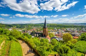 Kleine Stadt mit Kirchturm inmitten grüner Hügel unter blauem Himmel mit vereinzelten weißen Wolken